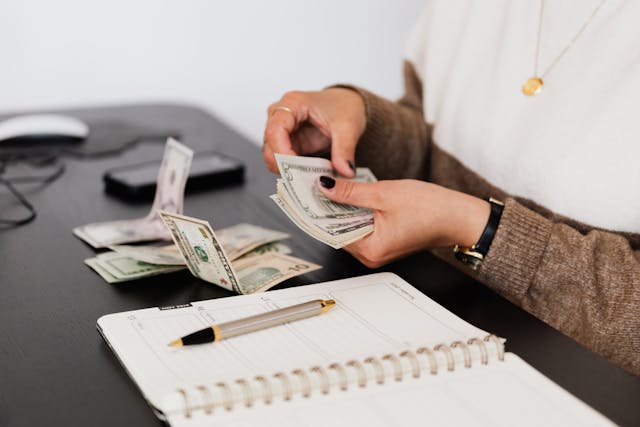 Person counting money with both hands over a notebook on a table